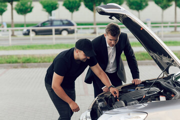 Fototapeta na wymiar A young car dealer in a business suit shows buyers a new car. Young man buy a car. Seller and man inspect the hood of the car. Purchase of machines, test drive