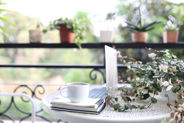 Coffee cup and laptop and notebook with tokyo snow plant on white metal table at balcony