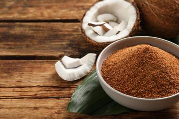 Natural coconut sugar in bowl on wooden table, space for text