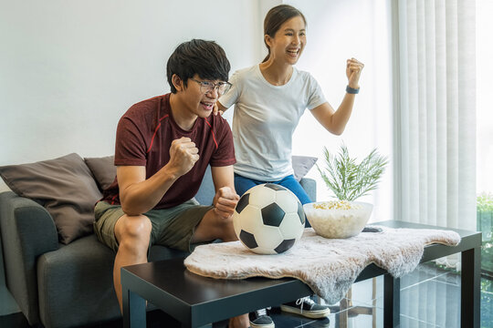 Football Supporters Having Fun And Celebrate During Watching Football Game On Television At Home. Asian Friends Fans Cheering Live Soccer Game.