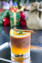 iced americano black coffee , orange juice on top a slice orang with rosemary, cinnamon on stainless steel saucer and colorful gift box background. summer caffeinated beverages