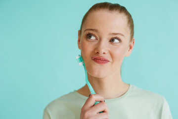 Young blonde woman looking upward while posing with toothbrush