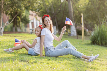 Patriotic holiday. Happy family, mother and daughter with American flag outdoors on sunset. USA...