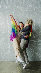Positive young women with dreadlocks dancing and holding rainbow flag isolated in studio