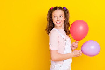 Photo portrait schoolgirl with tails keeping air balloons looking copyspace isolated vivid yellow color background