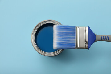 Can of paint and brush on light blue background, top view