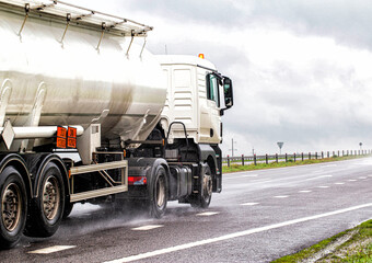 A white semitrailer tractor with a stainless tanker truck transports dangerous goods on the road. Kotsnet transportation of engine oil and diesel fuel to filling stations.  - obrazy, fototapety, plakaty