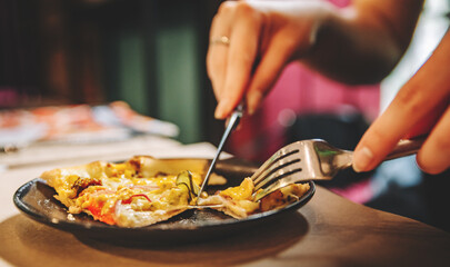 woman hands with knife and fork cutting pizza on table in cafe