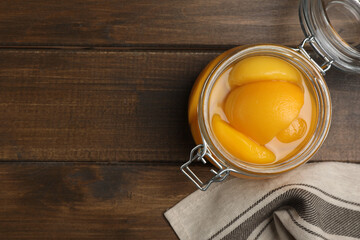 Canned peach halves in glass jar on wooden table, flat lay. Space for text