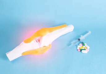 Knee joint mockup on a blue background and pills with a syringe. The concept of treatment of the...