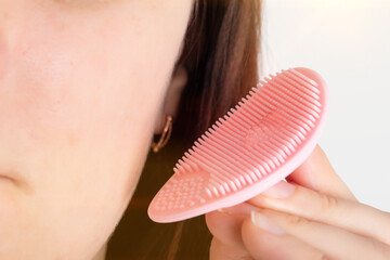 The girl holds a pink silicone brush near her cheek to clean the pores of the skin from pollution....