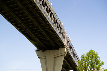View of the structure of the highway bridge from below against the light blue sky. The road passes over the city, over the green trees. Saint Petersburg, Europe