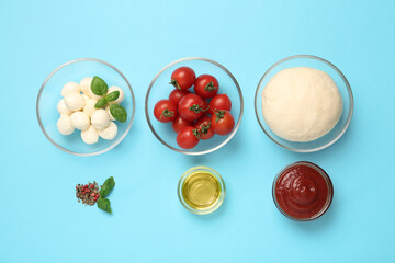 Raw dough and other ingredients for pizza on light blue background, flat lay