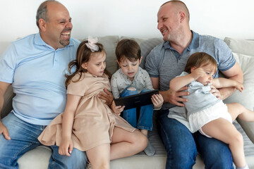 Cropped shot of an affectionate family of five using digital tablet on the sofa at home. Family reading on digital tablet together at home. Parents and kids using digital tablet at home. Copy space.
