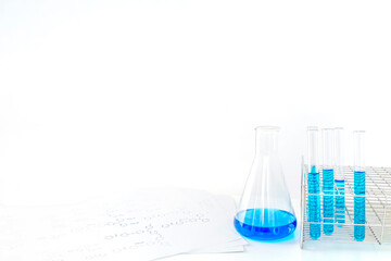 白背景に着色された溶液の入ったフラスコと試験管、テーブルに置かれた分子構造の資料