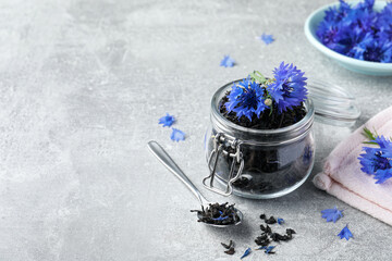 Dry tea leaves and cornflowers on light table. Space for text - obrazy, fototapety, plakaty
