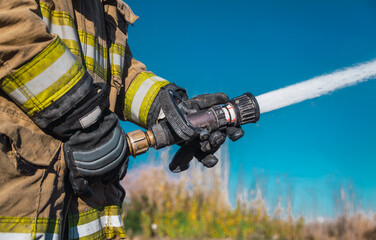 Fototapeta na wymiar Hands of firefighter, no face, holding a hose by throwing water at high pressure.