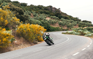 Fototapeta na wymiar biker riding on green motorbike taking a curve on a mountain road. 