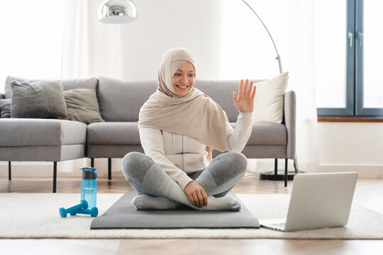 Middle Eastern Islamic Muslim Mature Woman In Hijab Having Video Conversation On Laptop Sitting On Exercise Mat After Hard Training Workout At Home, Watching Fitness Tutorial