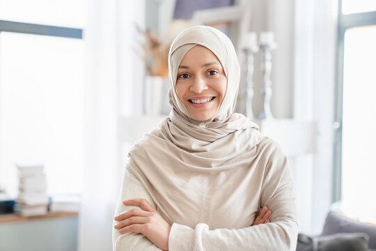 Confident mature Middle Eastern muslim islamic woman in hijab, mother, tutor, wife standing with arms crossed at home. Front view portrait of a arabian woman