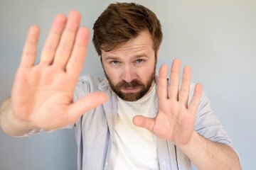 Confident fearless Caucasian man makes stop gesture, palms forward and looks seriously into camera....