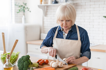 Senior old eldery aged woman grandmother cooking salad in kitchen at home. Grandma preparing food,...