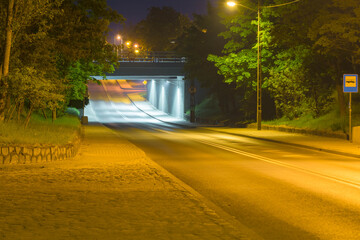 Asfaltowa droga przebiegająca pod wiaduktem kolejowym. Widok w nocy. 