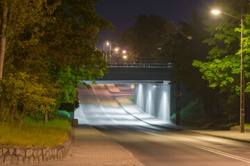 Asfaltowa droga przebiegająca pod wiaduktem kolejowym. Widok w nocy.  - obrazy, fototapety, plakaty