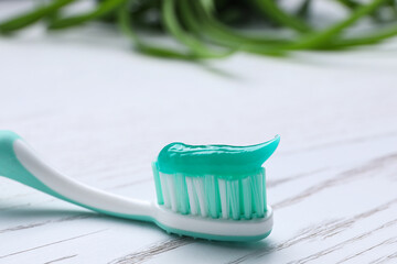 Brush with toothpaste on white wooden table, closeup