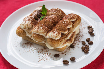 Homemade Italian tiramisu dessert with cocoa powder on a white plate on red napkin.