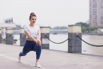 Runner stretching muscles outdoor at summer morning in city. Running athlete woman doing fitness stretch. Healthy young caucasian woman warming up outdoors before exercise.