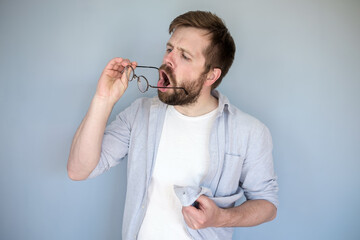 Young bearded Caucasian man cleans his glasses from dust and dirt, he breathes on the lenses and...