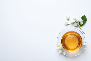 Glass cup of aromatic jasmine tea and fresh flowers on white background, top view. Space for text