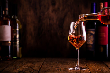 Wine tasting. Rose wine pouring into glass on wooden background with selection of red, white and...