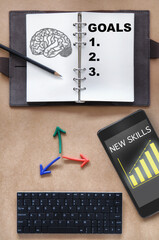 Brain drawing and goals written on organizer book with pencil, colorful arrow, new skills and growth graph on smartphone and mini keyboard on desk. Reskilling and upskilling machine learning concept