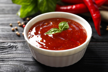 Spicy chili sauce with basil on dark wooden table