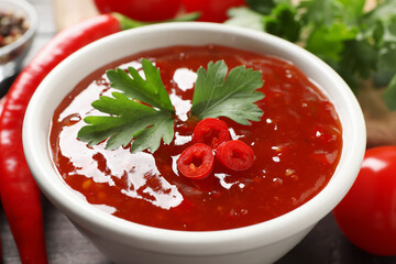 Spicy chili sauce with parsley on table, closeup