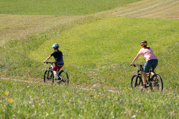 Mother and daughter riding mountain bikes in the country road in green nature on a sunny day.