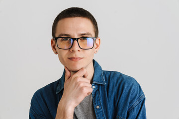 Young man in eyeglasses touching his chin and looking at camera