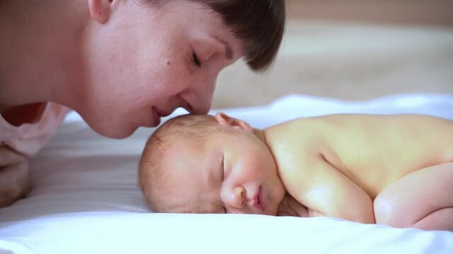 Little newborn child. Home family portrait. Mother kiss small son. Happy emotion. Lying in bed. Calm infant