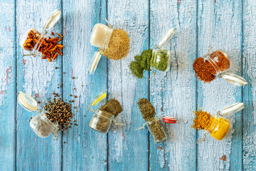 Airtight spice jars overturned on blue wooden background with pepper, oregano, cayenne, sesame, paprika, curry