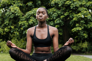 Young black woman doing meditation and yoga in a park. - obrazy, fototapety, plakaty