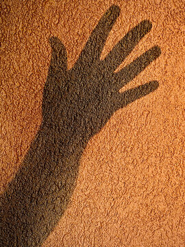 Shadow of a hand over an orange textured wall