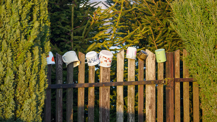 Colorful cups on a wooden fence among green trees.