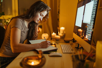 Busy woman working with computer and notebook in room with burning candles