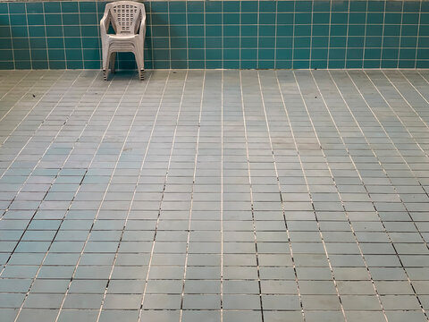 An empty tiled pool with plastic garden chairs piled inside it