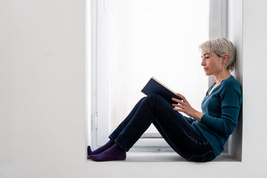 Woman reading book against window