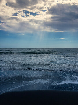 The sea, the blue sky, fluffy clouds and beams of light coming from above