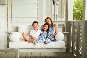 Little Brother and Sisters Sitting on Porch Swing