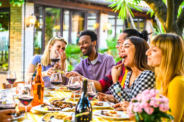 Group of happy multiracial friends having dinner in the restaurant garden -  Friendship concept with happy people having fun together toasting drinks and eat at terrace.